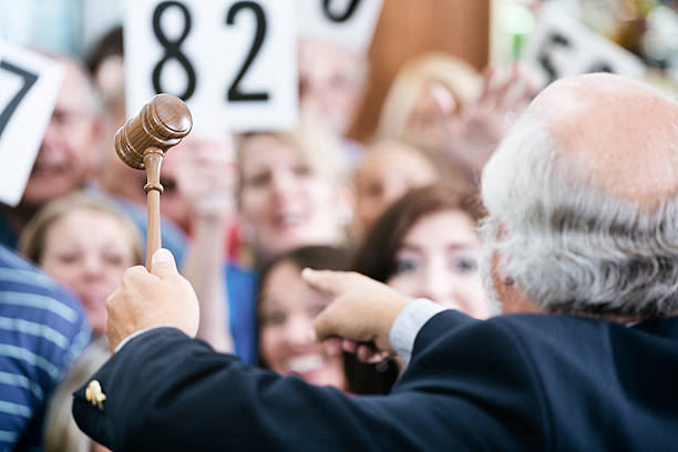 Auctioneer with Large Crowd of Buyers A crowd of bidders at an auction. The focus is on the auctioneer's gavel as he calls out bids. auction photos stock pictures, royalty-free photos & images