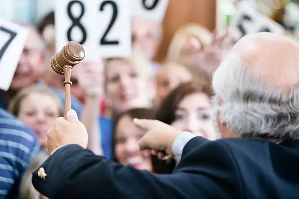 A crowd of bidders at an auction. The focus is on the auctioneer's gavel as he calls out bids.