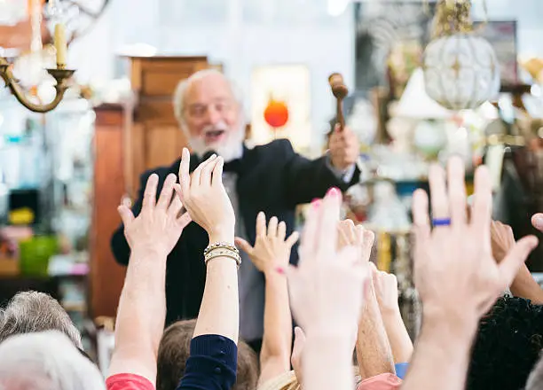 A crowd of bidders at an auction. The focus is on the bidder's hands as he calls out bids.