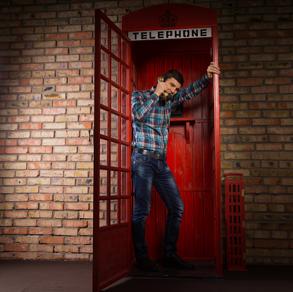 Man standing chatting in a replica red British phone booth standing leaning against the open door, full length view