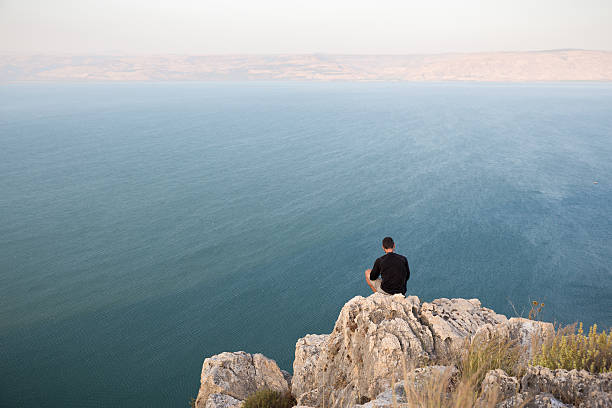 istock Man sitting stone cliff above lake sea. 478639602