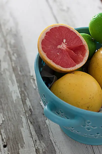 open and eaten grapefruit in a blue fruitbowl with limes on a weathered picnic table.