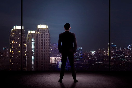 Man standing in his office looking at the city at night. Business success concept