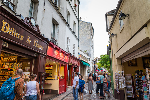 Paris, France - September 25, 2013: Montmartre street scene in the city's 18th arrondissement, where tourists and locals can be seen on the cobblestone streets. Shops and restaurants are visible on both sides of the street. This historic district used to be a village but was annexed to Paris in 1860. 