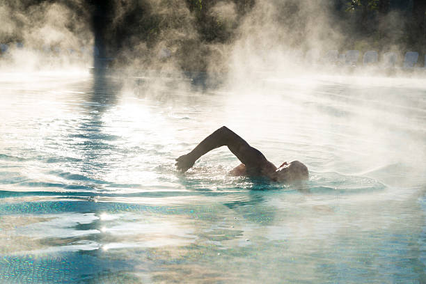 Silhouette of man swimming as steam rises from pool.