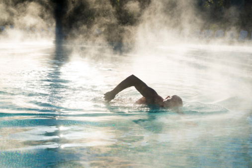 Silhouette of man swimming as steam rises from pool.