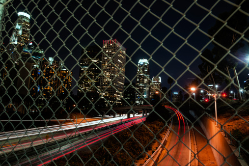 Overview of traffic on the freeway at night through a wire fence.