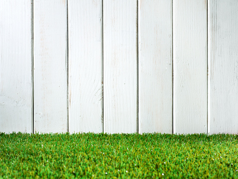 This is a close up photo of a white fence in a backyard. This photograph will work well as a background to add copy space on top of.