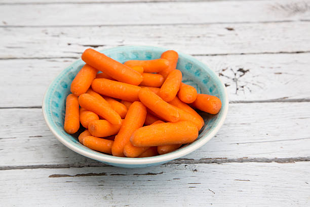 istock Baby carrots in bowl on white wood 478662464