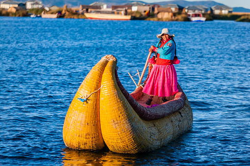 Peruvian woman sailing between Uros floating islands. Uros are a pre-Incan people that live on forty-two self-fashioned floating island in Lake Titicaca Puno, Peru and Bolivia. They form three main groups: Uru-Chipayas, Uru-Muratos  and the Uru-Iruitos. The latter are still located on the Bolivian side of Lake Titicaca and Desaguadero River. The Uros use bundles of dried totora reeds to make reed boats (balsas mats), and to make the islands themselves. The Uros islands at 3810 meters above sea level are just five kilometers west from Puno port.http://bem.2be.pl/IS/peru_380.jpg