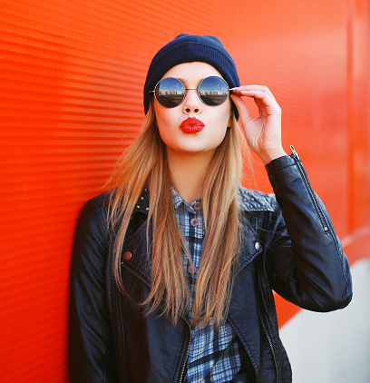 Portrait of fashionable blonde girl with red lipstick wearing a rock black style having fun outdoors in the city