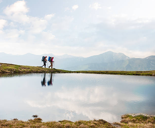Trekkers passing by a calm lake in the mountains stock photo