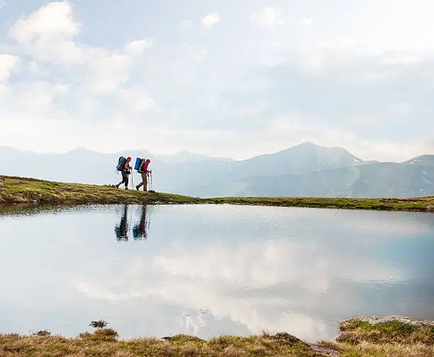 Photo of Trekkers passing by a calm lake in the mountains
