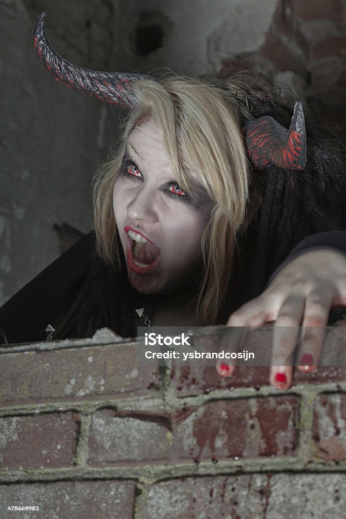 Scary hungry female demon crawling over old dirty brick wall. Adult Stock Photo