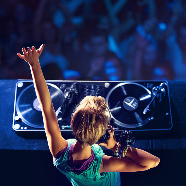 She makes the crowd go wild! Rear-view shot of a trendy young DJ mixing up some music with a crowd in the background dj stock pictures, royalty-free photos & images