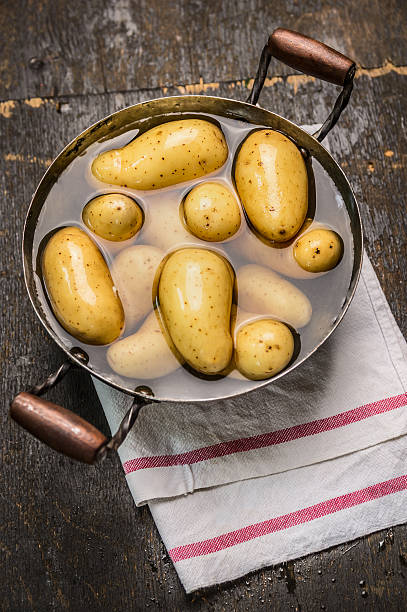 New potatoes in old pan with water on rustic wooden