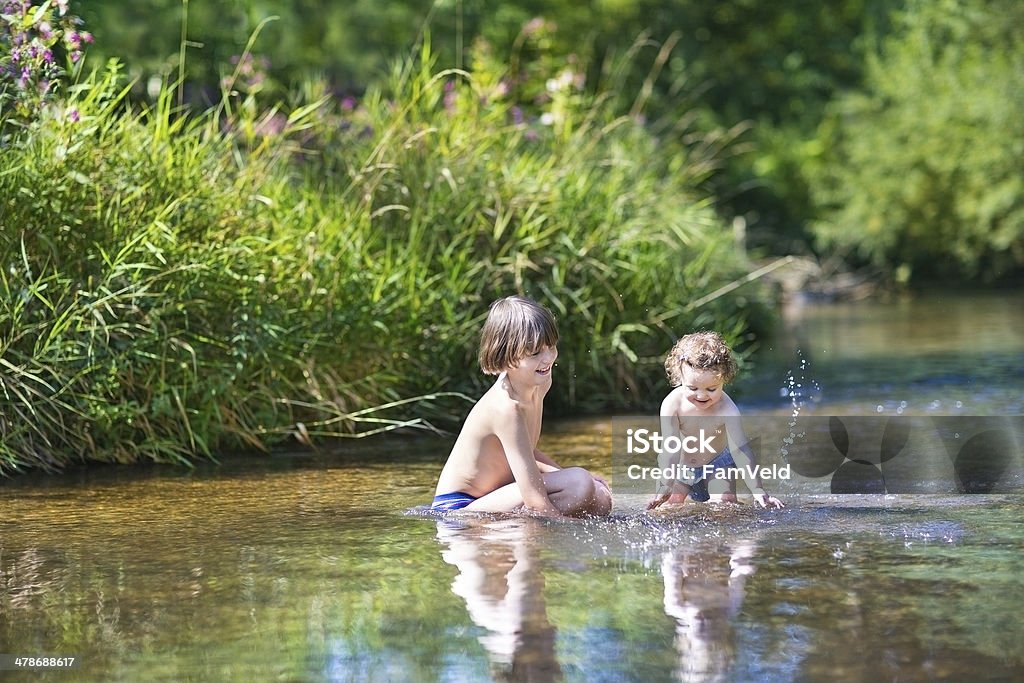 Young cute boy and his baby sister playing in river Young cute boy and his little baby sister playing in the water in a beautiful river on a sunny summer day River Stock Photo