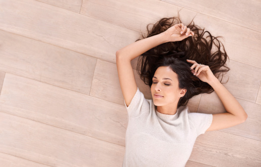 Studio shot of a beautiful young woman lying on a wooden floor with her arm above her head