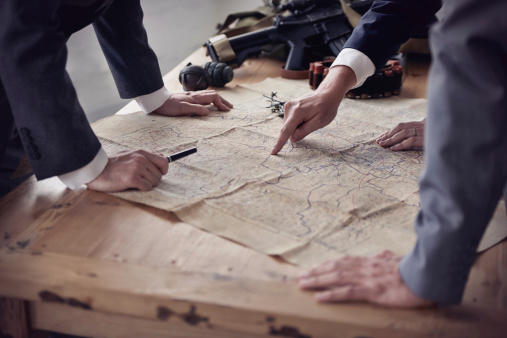 Three men in suits discussing plans while looking at a map lying on a table