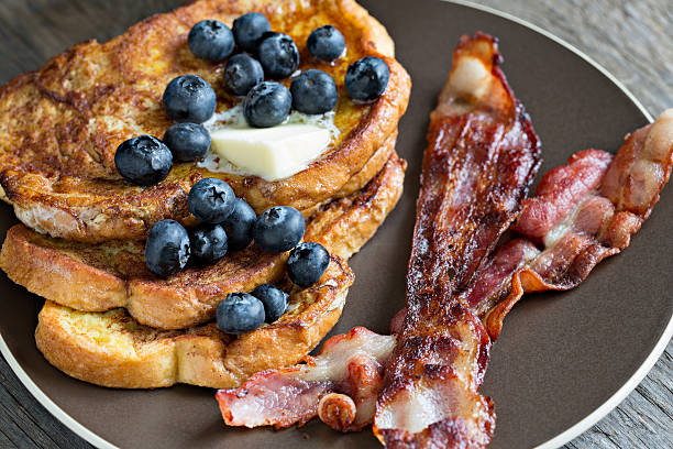 Bacon And French Toast A high angle extreme close up shot of a stack of french toast and several bacon strips. french toast bacon bread butter stock pictures, royalty-free photos & images