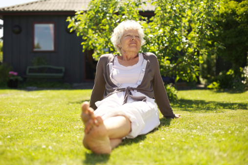 Senior woman sitting relaxed on grass in backyard garden outdoors