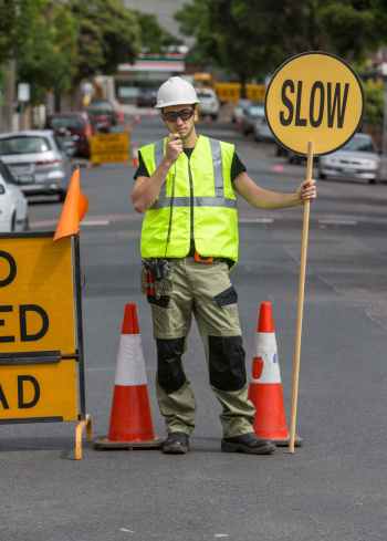 worker talking to radio and holding slow sign in the street, with traffic cones around him