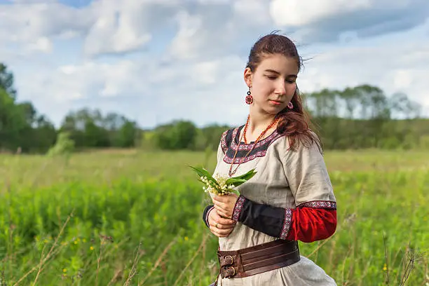 Sad cute farmgirl looking back on a summer field, wearing traditional dress, holding harebells flowers