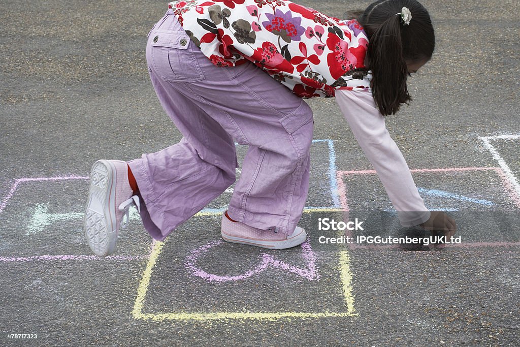 Girl Playing Hop-Scotch In Playground Side view of young girl playing hop-scotch in playground Balance Stock Photo