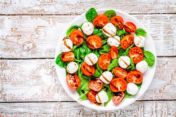 salad of mozzarella, cherry tomatoes and spinach with balsamic sauce salad of mozzarella, cherry tomatoes and spinach with balsamic sauce on a white rustic table caprese salad stock pictures, royalty-free photos & images