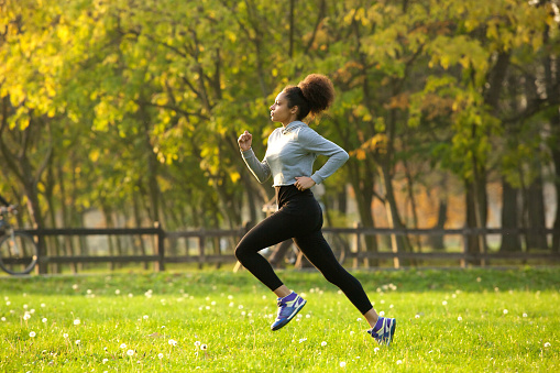 Side view full body portrait of a young woman jogging outdoors