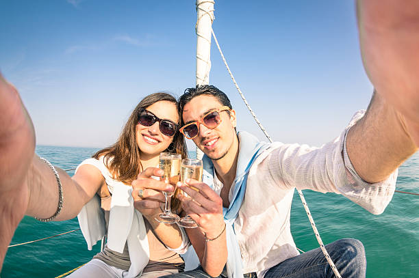Young love couple taking selfie on sailing boat with champagne Young couple in love taking selfie on sailing boat cheering with champagne wine - Happy jubilee party cruise travel on luxury sailboat with boyfriend and girlfriend - Bright sunny afternoon color tone yacht selfie stock pictures, royalty-free photos & images