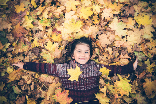 Toddler having fun lying down on fallen leaves