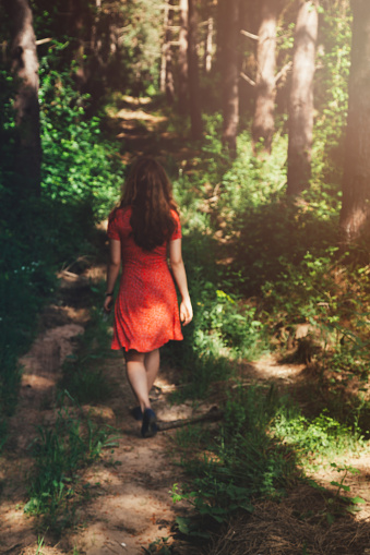 Young woman in red dress walking and having fun on forest alley