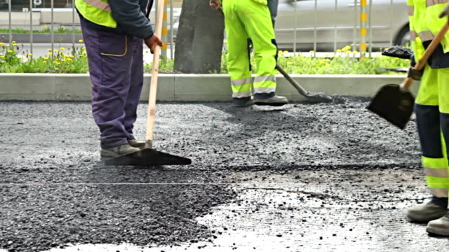 Road construction workers leveling asphalt on the new road
