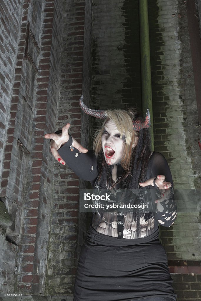 Scary female demon in front of old dirty brick wall. Adult Stock Photo