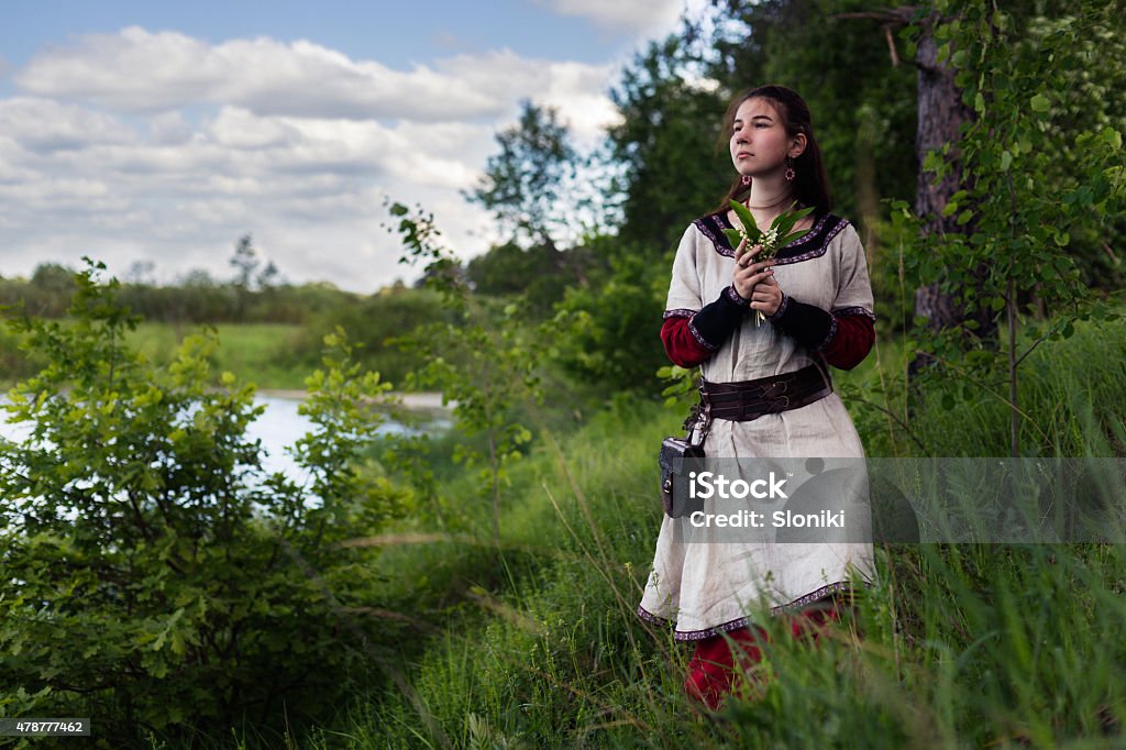 Sad pretty farmgirl looking far away near river. Sad cute farmgirl looking far away near river, wearing traditional dress, holding harebells flowers. 2015 Stock Photo