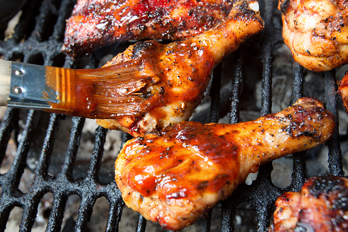 Half dozen chicken legs cooking on an old fashioned back yard charcoal barbecue grill with red hot coals underneath.  Chicken has been marinated, seasoned and glazed with barbecue sauce and is ready to serve with a final basting of barbecue sauce with a brush.Half dozen chicken legs cooking on an old fashioned back yard charcoal barbecue grill with red hot coals underneath.  Chicken has been marinated, seasoned and glazed with barbecue sauce and is ready to serve.