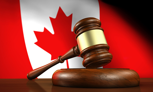 Law and justice of Canada concept with a 3d rendering of a gavel on a wooden desktop and the Canadian flag on background.