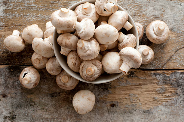 Fresh whole white button mushrooms Fresh whole white button mushrooms, or agaricus, in a bowl on a rustic wooden counter ready to be cleaned and washed for dinner, overhead view comprehensive stock pictures, royalty-free photos & images