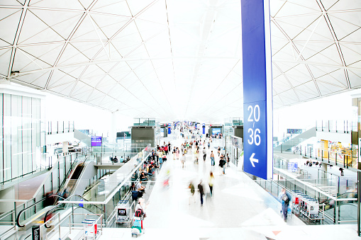 A view of a busy airport interior, people travelling, motion blurred and high key. Contemporary architecture, horizontal composition. 