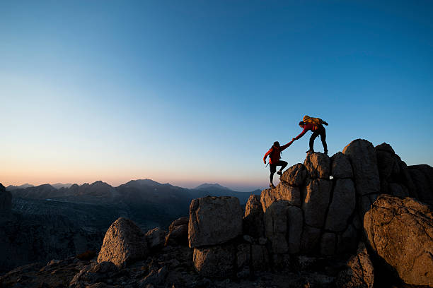 pure adventure Pair of climbers, one helping the other to the summit of a peak  rock climbing stock pictures, royalty-free photos & images