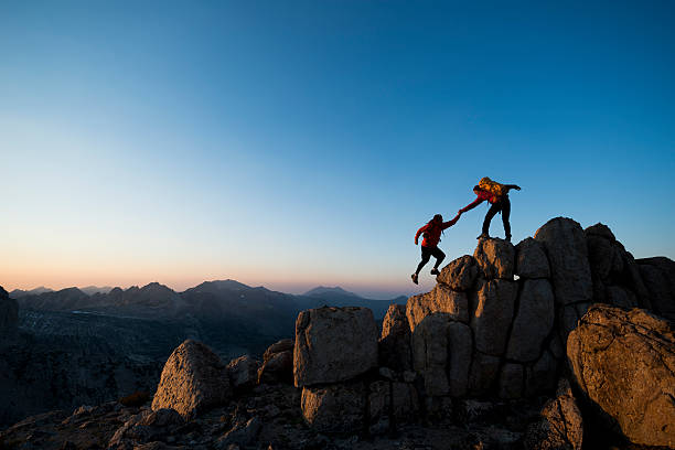 climbing to the top One climber helping the other get to the top of a mountain  rock climbing stock pictures, royalty-free photos & images
