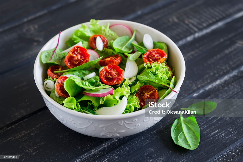 salad with fresh vegetables, garden herbs and sun-dried tomatoes salad with fresh vegetables, garden herbs and sun-dried tomatoes in a white bowl on a dark wooden background Salad Stock Photo