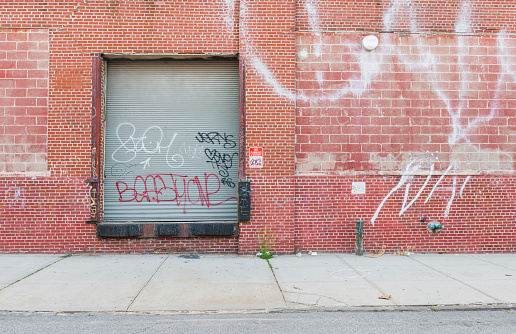 This is a horizontal, color, royalty free stock photograph of a closed, gray, metal, industrial door in Williamsburg Brooklyn. The simple architectural feature of this commercial property is set in an exterior, red brick wall. Photographed with a Nikon D800 DSLR Camera.