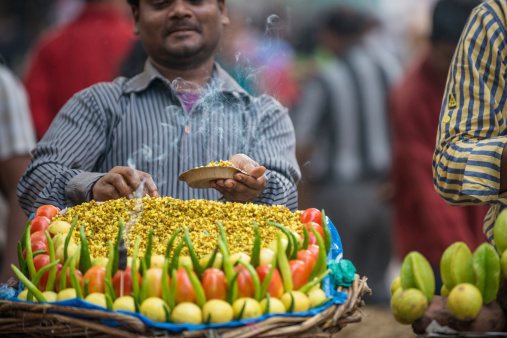 New Delhi, India - November 8, 2013: A street food vendor prepares mung bean chaat with tomatoes, lemon and green chilies.  The vendor to the right is preparing sweet potato and starfruit chaat.