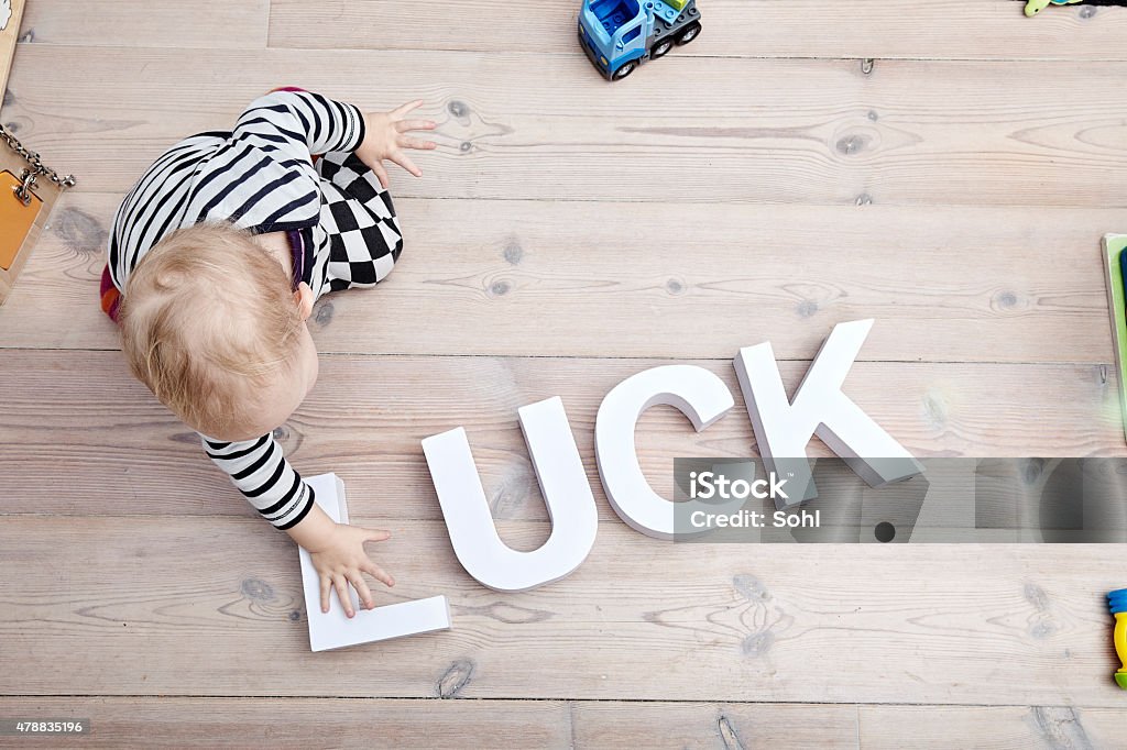 Lucky Kid Luck written in white letters on the floor of a house / apartment. A small child sitting and touching some letters - there is lying toys round on the floor 2015 Stock Photo