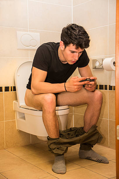 istock Young Man with Cell Phone Sitting on Toilet 478838060