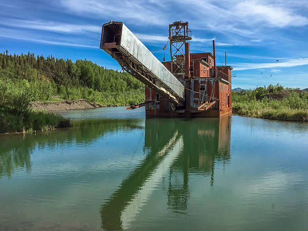 Historical Alaskan gold dredge in a river with a reflection