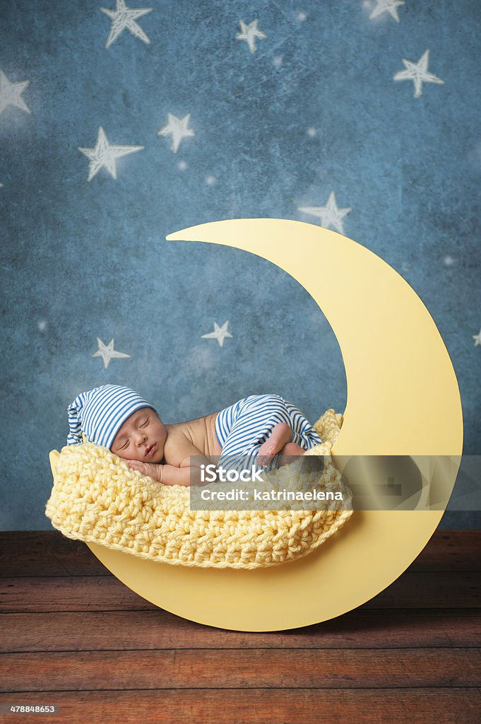 Newborn Boy Sleeping on the Moon Studio portrait of a nine day old baby boy wearing pajama bottoms and a sleeping cap. He is sleeping on a moon shaped posing prop. Baby - Human Age Stock Photo