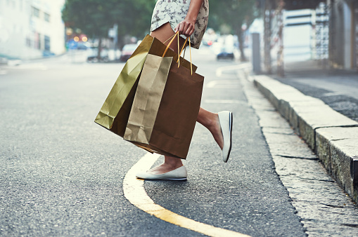 Cropped shot of a woman with shopping bags crossing a city street